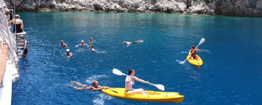Families swimming and kayaking in the sea beside a traditional wooden gulet