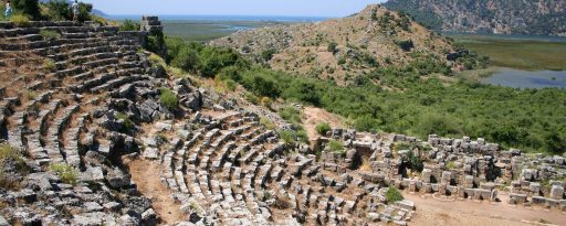View into the ancient theatre with a few travellers admiring the view out to sea at the archaeological site of Kaunos in Turkey