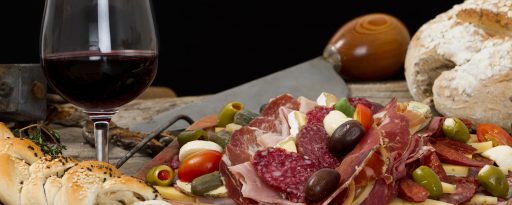 A close up of traditional antipasti, salamis, olives, bread and more with a glass of red wine during a meal in Sicily, Italy