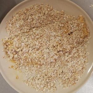 Still step 4: the floured fillet has been pulled through the egg mixture and is now being coated with oatmeal.