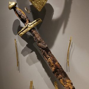 Detail from the display of (male) Grave 131. The iron sword has gold decorations, there is also a golden finger-ring, a wrist-cover and smaller ornaments probably sewn to body armour (or a shroud?).