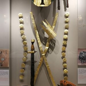 Full display of (male) Grave 480, with 'Illyrian' helmet richly adorned with gold, an unusual decorated gold face-cover, two iron swords with gold decoration, two iron spearheads, gold rosettes from armour or clothing, a complex gold cover for wrist and fingers, gold bands that decorated the straps of a composite shield, imported pottery including a perfume flask in the shape of a sandalled foot and an Attic 'eye cup'. Circa 550-540 BC.
