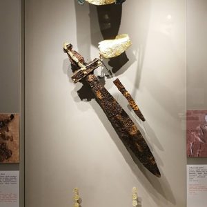 The full display of (male) Grave 9, with helmet, gold stomion (mouth cover), golden wrist-cover, iron sword, dagger, clothing ornaments and clay vessels in animal shape. Circa 550 BC.