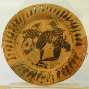 A black-figure plate depicting one armed hoplite warrior pursuing another, ca. 500 BC. A fitting offering from the tumulus of the Athenians who fell in the 490 BC Battle of Marathon. Marathon Museum.
