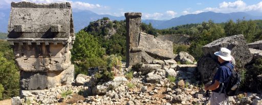 A man looking at the ancient tombs with mountains in the background at the archaeological site of Pinara in Lycia, Turkey