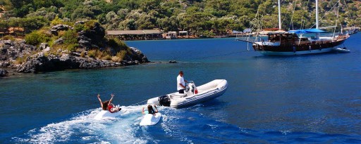 Children having fun being pulled behind a dinghy on the sea with a traditional gulet in the background