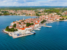 Aerial panorama of the Old Town of Poreč, Croatia, featuring its historic red-tiled buildings on a peninsula, the Euphrasian Basilica bell tower, and the BO Hotel Palazzo at the tip, surrounded by the blue Adriatic Sea.