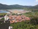 Aerial view of the town of Ston, Croatia, showing its historic buildings with red-tiled roofs famous salt pans set out in a grid pattern and lush green hills.