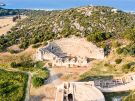 Aerial view of the ancient theatre and ruins of Patara, Turkey, with lush green hills and the Mediterranean coastline in the background.