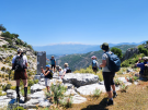 A group of hikers standing near the 2500 year old pillar tomb at the entrance to the ancient city of Sidyma on the Lycian Way, Turkey, with a scenic mountain backdrop.