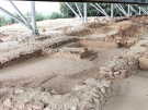 Excavated remains of the 3,200-year-old Palace of Nestor in Pylos, Greece. The image shows the low stone foundations of various rooms and corridors, all protected by a modern, high-reaching metal canopy with white support beams.