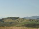Rolling green and yellow agricultural hills under a pale blue sky in the countryside near Aidone and Morgantina in central Sicily.