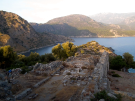 Elevated view of Byzantine church ruins on Gemiler Island, Turkey, overlooking a calm blue bay and rocky mountains at sunset.