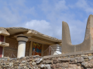The Horns of Consecration monument at the Palace of Knossos in Crete, with reconstructed Minoan columns and a fresco in the background.