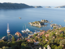 High-angle panoramic view looking down from Simena Castle onto Kaleköy harbor with yachts, traditional stone houses, and the blue Mediterranean Sea in Antalya, Turkey.
