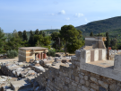 Wide view of the Palace of Knossos ruins in Crete, highlighting the stone foundations, the North Bastion, and green Mediterranean hills.