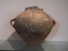 Reassembled ancient terracotta pithos storage jar decorated with a black painted fish-scale or wave geometric pattern, on display at the Museo Archeologico di Aidone in Sicily.