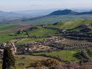 Panoramic high-angle view of the lush green valleys, olive groves, and winding dirt roads in the countryside surrounding Morgantina and Aidone, Sicily.