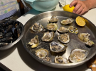 A view of a seafood meal featuring a metal platter of freshly shucked Mali Ston oysters and a cooked lemon and a metal bowl of steamed mussels.