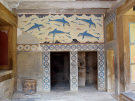 The Queen's Megaron at the Palace of Knossos, featuring the famous Minoan dolphin fresco above stone doorways with blue spiral borders.