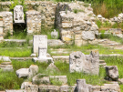 Ruins of the Sanctuary of Zeus Hypsistos in ancient Dion, featuring stone walls, marble bases with eagle carvings that were the symbol of Zeus, and a headless seated statue in a niche.