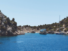 Several tourist double-decker yachts and a sailboat anchored in the calm turquoise waters of Tersane Bay on Kekova Island, Turkey.