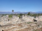A view from up on the citadel of Tiryns in Greece, from its interior towards green fields and distant mountains . In the foreground, the low foundations of dog-legged walls form what look like narrow corridors and galleries.