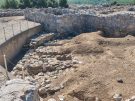 A view into the foundations of part of the Mycenaean palace citadel of Tiryns in Greece with two layers of ancient walls of largeish, roughly-shaped stones forming straight lines with gallery like rooms.