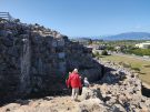 Some people walking down the west stairs at Tiryns in Greece from near the top. The citadel is on the left, marked by grey masonry, large stones imposingly forming the walls, packed with smaller ones at the interstices.