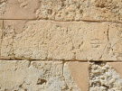 Close-up of ancient limestone wall blocks featuring faint Minoan mason's marks, including a carved trident symbol.